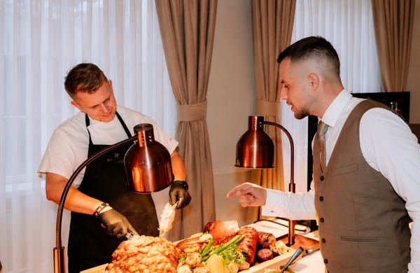Chef carving roast meat with a waiter at the buffet